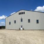 A stone grey post-frame riding arena with three overhead doors