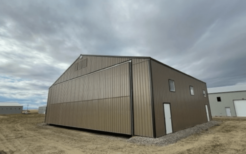A buckskin post-frame airplane hangar with a bi-fold door