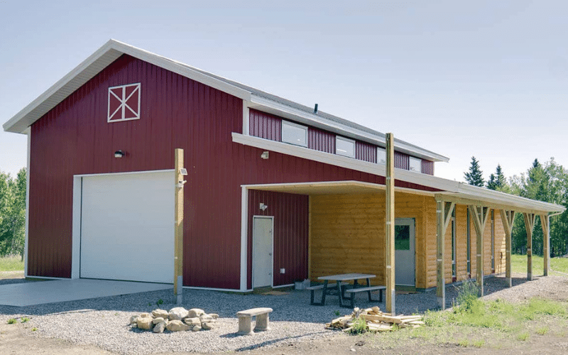 A dark red post-frame agricultural barn with one overhead door