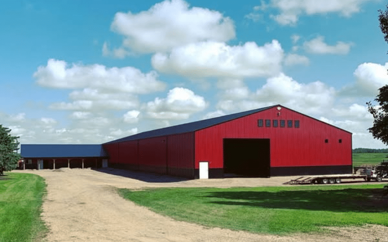 A dark red post-frame riding arena with three overhead doors and wainscoting