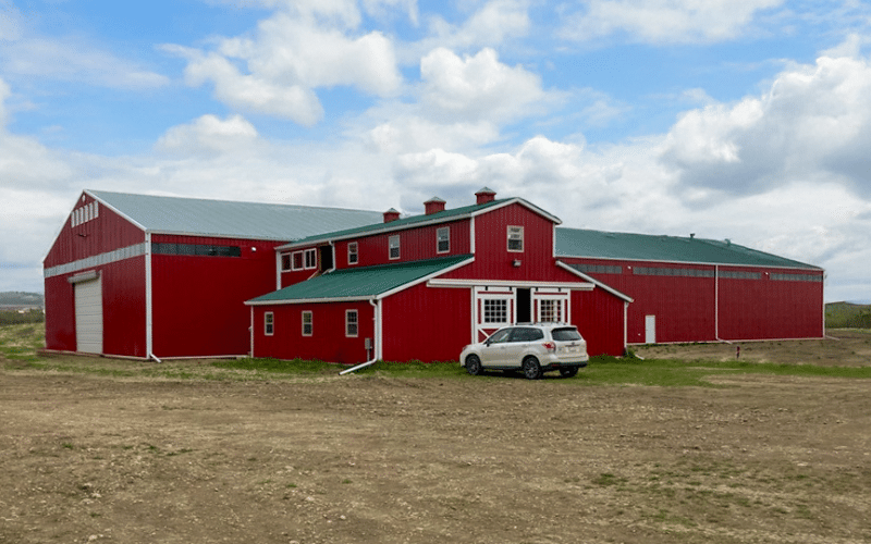 A bright red post-frame riding arena with three overhead doors and multiple cupolas