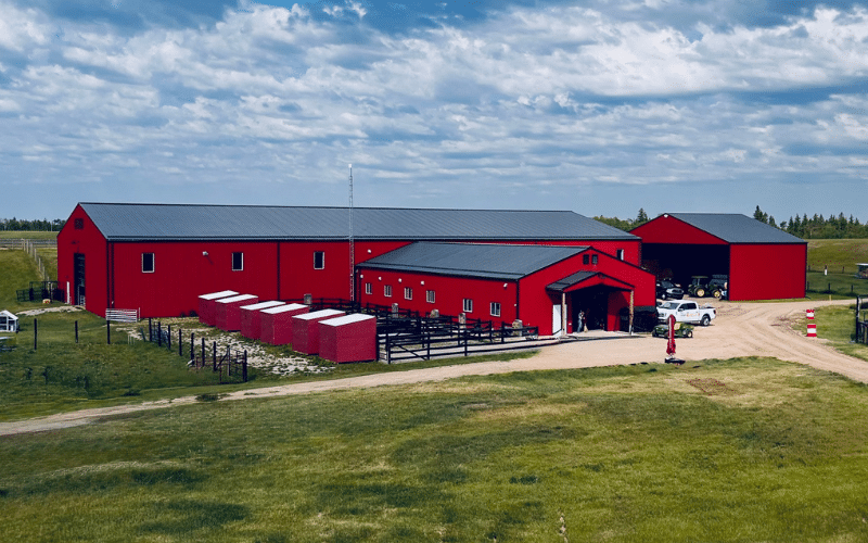 A dark red post-frame riding arena with soffits, overhead doors, and sliding doors