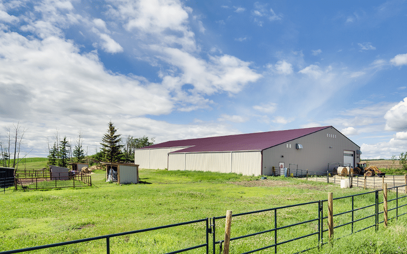 A stone grey post-frame riding arena with three overhead doors