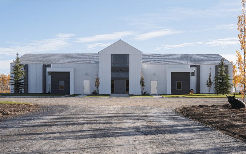 A bright white post-frame riding arena with a sliding door, and two overhead doors