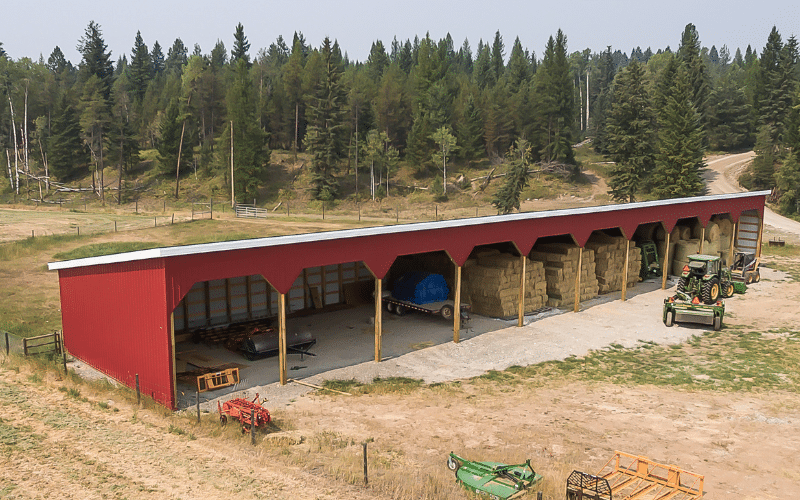 A dark red half open post-frame livestock shelter