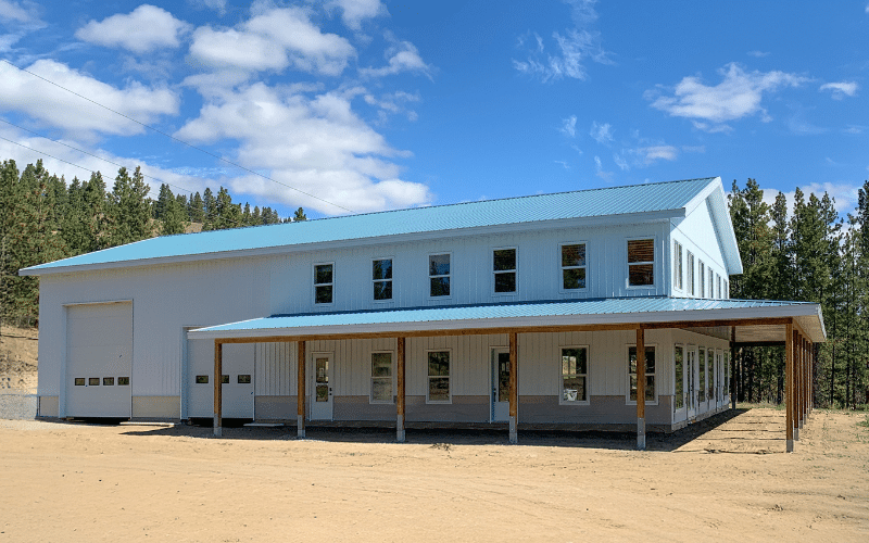 A bright white post-frame residential style shouse with overhead doors, soffits, and an open lean-to