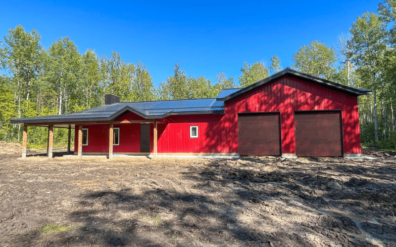 A dark red post-frame highwood with garage with two overhead doors, soffits, and open lean-tos