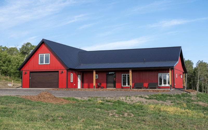 A dark red post-frame highwood with loft with an overhead door, front porch, and soffits