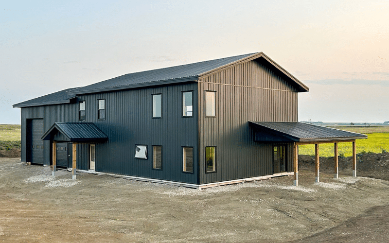 A iron ore post-frame custom residential building with open lean-tos, a wrap around porch, soffits, and overhead doors