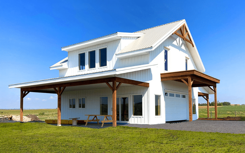 A bright white post-frame carriage house with open lean-tos, one overhead door, timber accents, and soffits