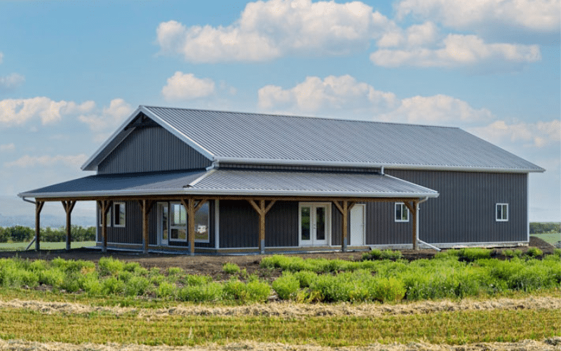 A charcoal post-frame Shouse with two open lean-tos, one overhead door, a porch, and soffits