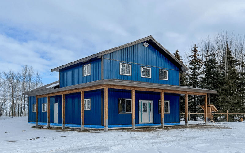 A heron Blue post-frame barndominium with open lean-tos, soffits, and one overhead door