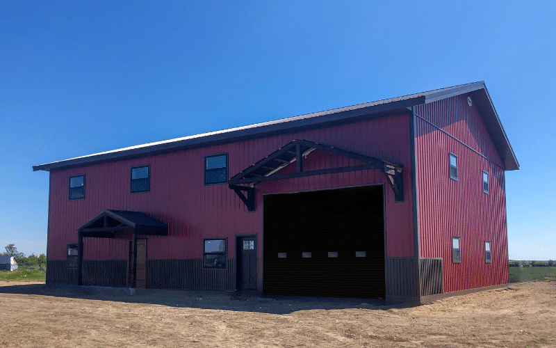 A Tile red post-frame shouse with wainscoting, timber accents, soffits, and closed lean-to