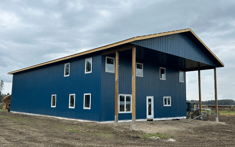A heron blue post-frame shouse with an open lean-to and soffits