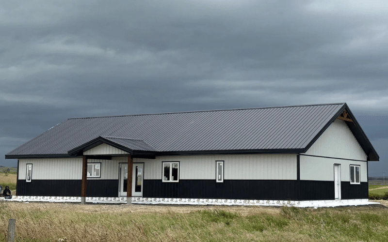 A white white post-frame Bunk House with timber accents, open lean-to porch, and black soffits