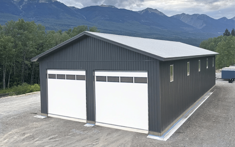 A charcoal post-frame agricultural storage building with two overhead doors and soffits
