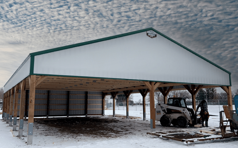 A white white post-frame agricultural storage building with open walls, and a melchers green roof