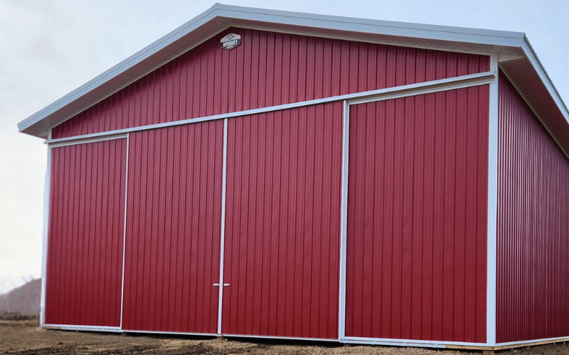 A dark red post-frame agricultural storage building with a sliding door and soffits