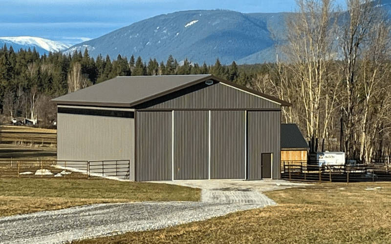 A charcoal post-frame agricultural storage building with soffits and a sliding door