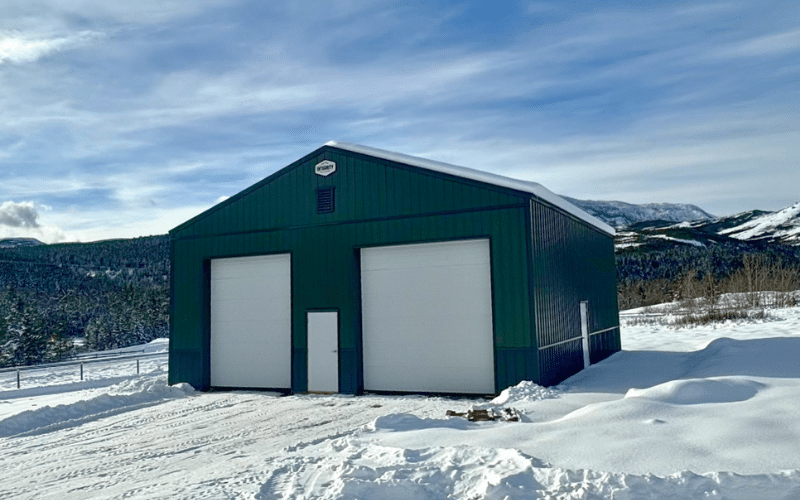 A dark sage post-frame agricultural storage building with overhead doors and wainscoting
