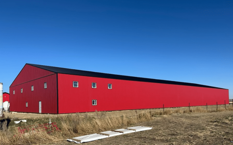 A bright red post-frame equestrian barn with overhead doors and a black roof