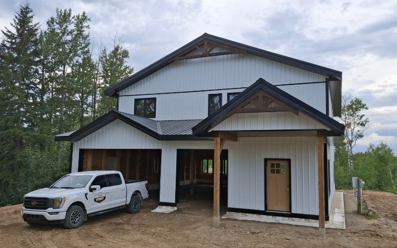 A bright white post-frame carriage house with a covered porch, closed lean-tos and a yellow front door