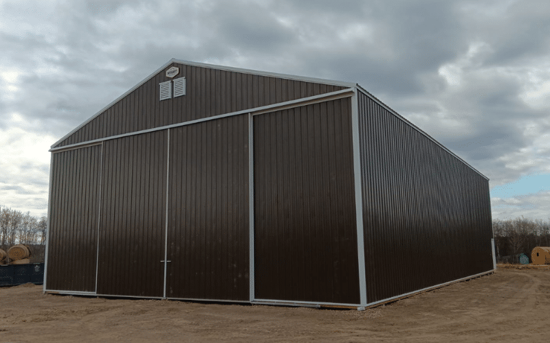 A coffee brown post-frame equestrian hayshed with sliding doors and overhead doors