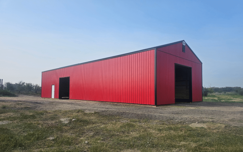 A bright red post-frame equestrian barn with sliding doors and overhead doors