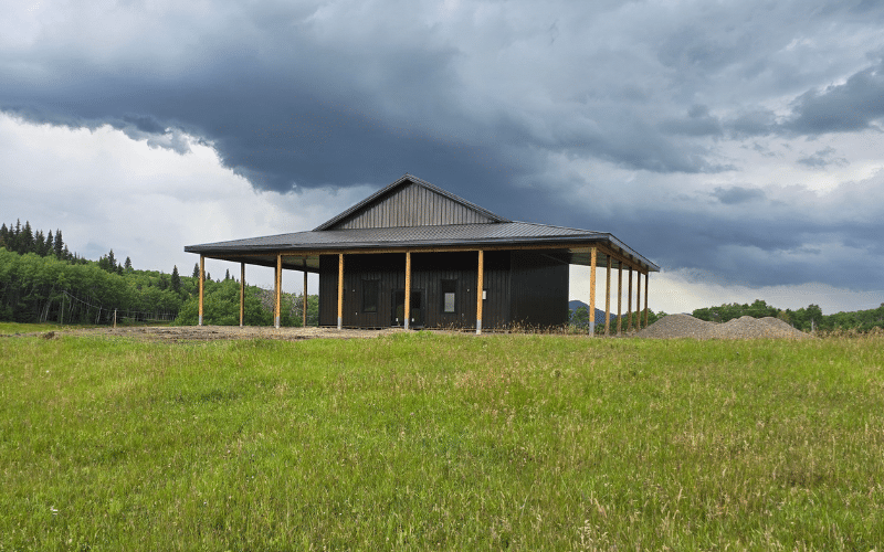 A coffee brown post-frame agricultural shop with wrap around open lean-to and overhead doors