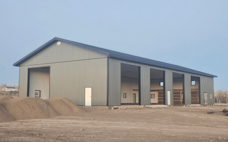 A dark sage post-frame agricultural shop with five overhead doors and soffits