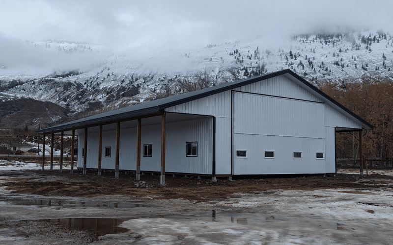 A bright white post-frame lifestyle & hobby shop with two open lean-tos, soffits, and overhead doors