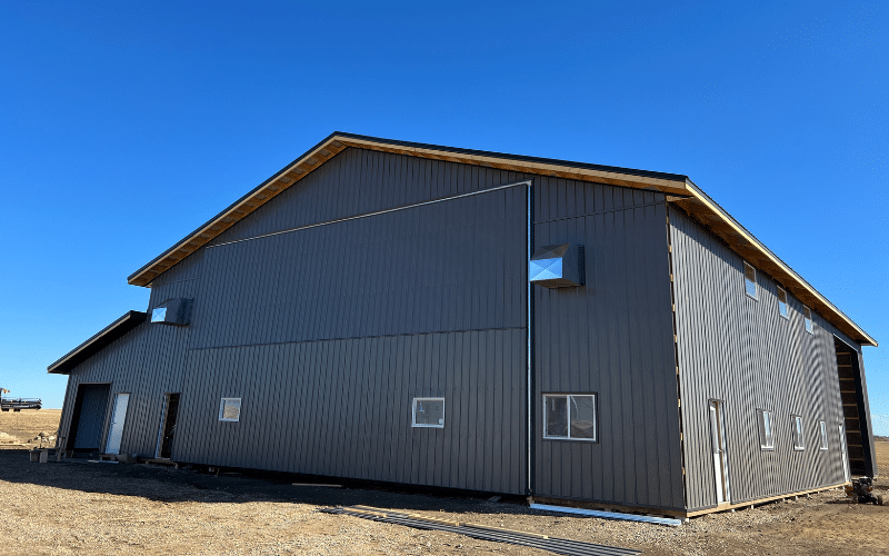 A charcoal post-frame agricultural shop with overhead and bi-fold doors, plus soffits