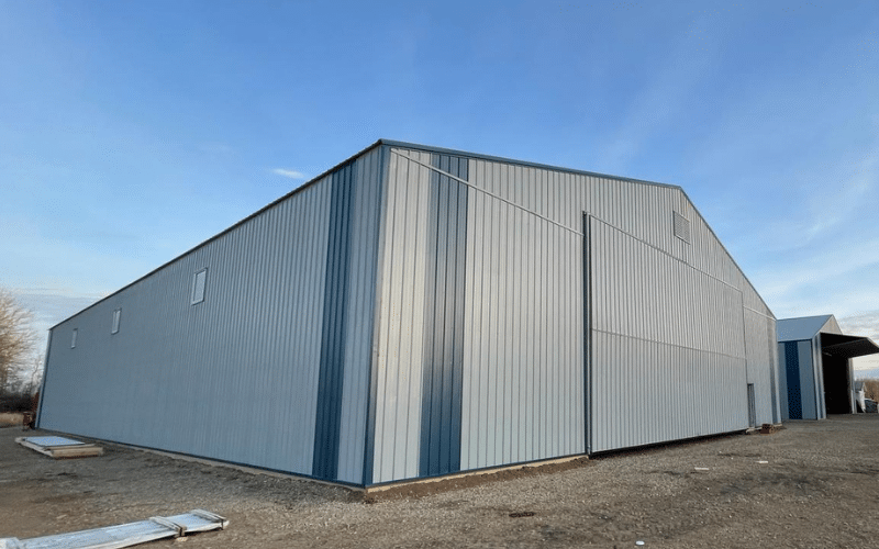 A regent grey post-frame agricultural Machine Shed with heron blue accents, and a bi-fold door