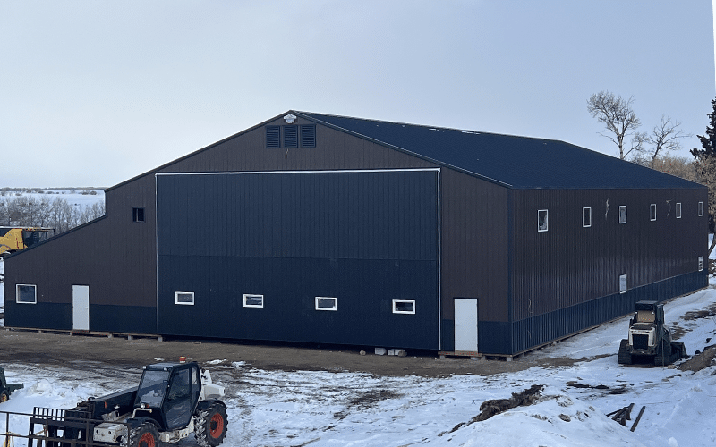 A coffee brown post-frame agricultural storage building with iron ore wainscoting, bi-fold and overhead doors.