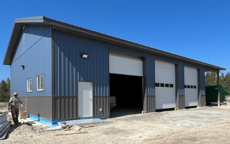 A blue bird post-frame agricultural shop with overhead doors, soffits, and charcoal wainscoting