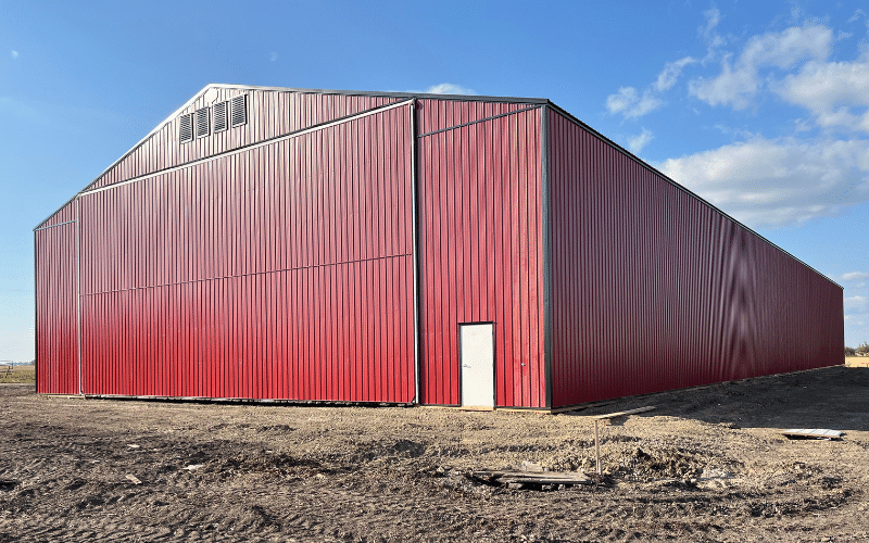 A dark red post-frame agricultural Machine Shed with a bi-fold door and black roof