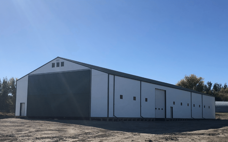 A bright white post-frame equestrian barn with melchers green roof and bi-fold door.