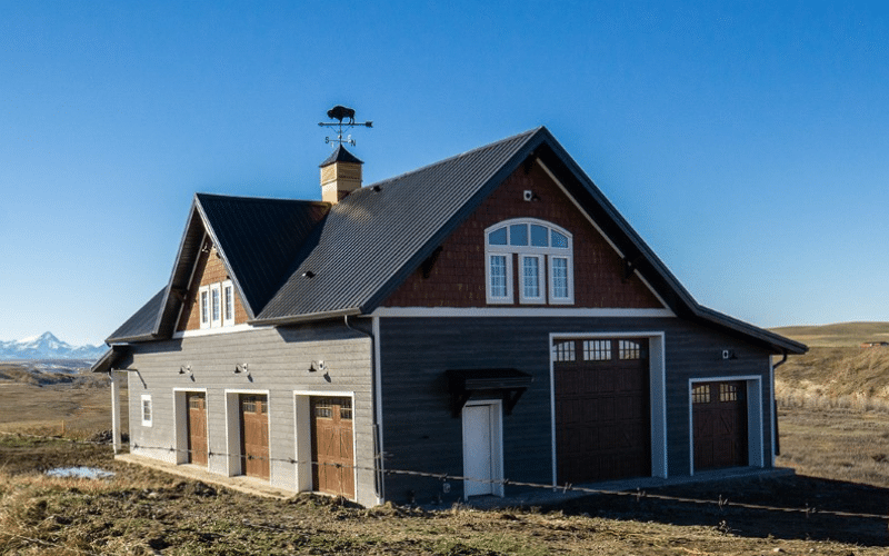 An iron ore post-frame equestrian barn with closed lean-to, a front porch, cupola, overhead doors and soffits