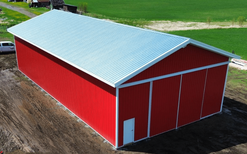 A bright red post-frame agricultural storage building with sliding doors and soffits