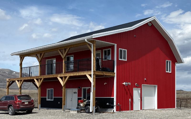 A bright red post-frame equestrian barn with an open lean-to, soffits and one overhead door