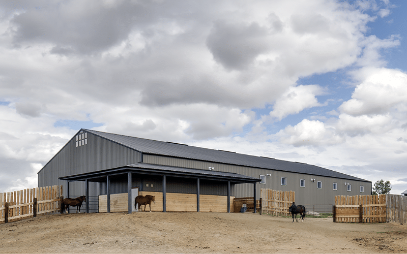 A sable post-frame riding arena with overhead doors, an open lean-to and kickwall