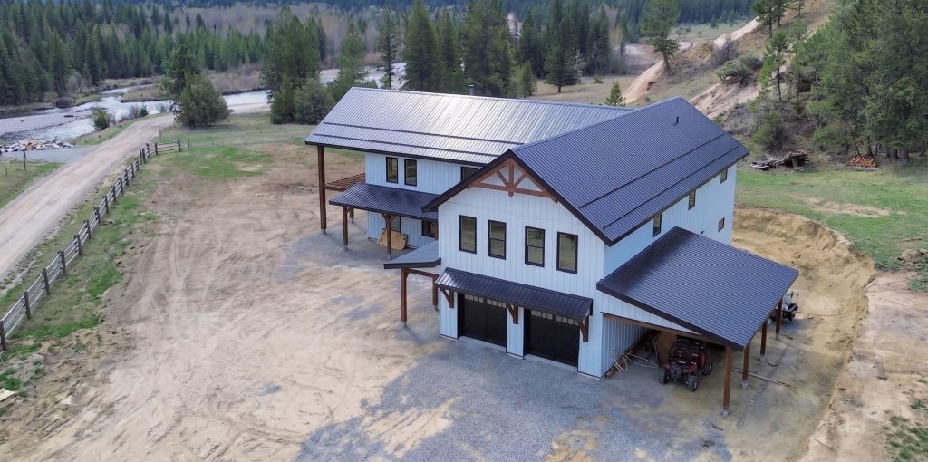 A bright white post-frame residential style Barndominium with three open lean-tos and two overhead doors