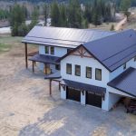 A bright white post-frame residential style Barndominium with three open lean-tos and two overhead doors