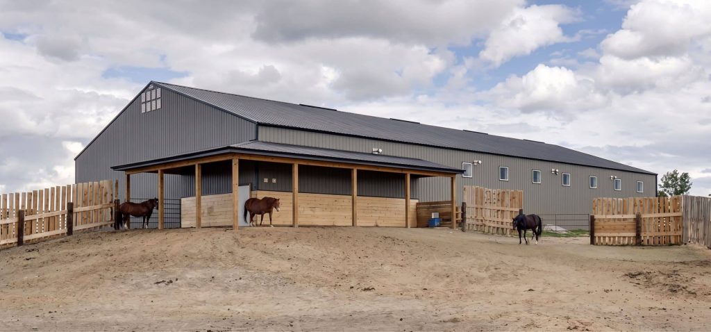 A sable post-frame riding arena with overhead doors, an open lean-to and kickwall