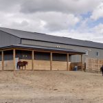 A sable post-frame riding arena with overhead doors, an open lean-to and kickwall