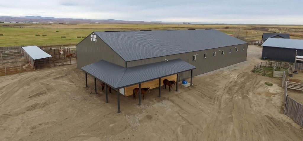 A sable post-frame riding arena with overhead doors, an open lean-to and kickwall