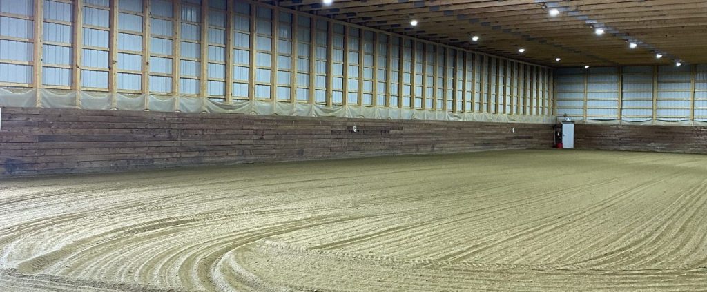 A stone grey post-frame riding arena with three overhead doors