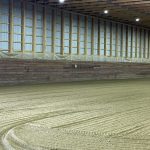 A stone grey post-frame riding arena with three overhead doors