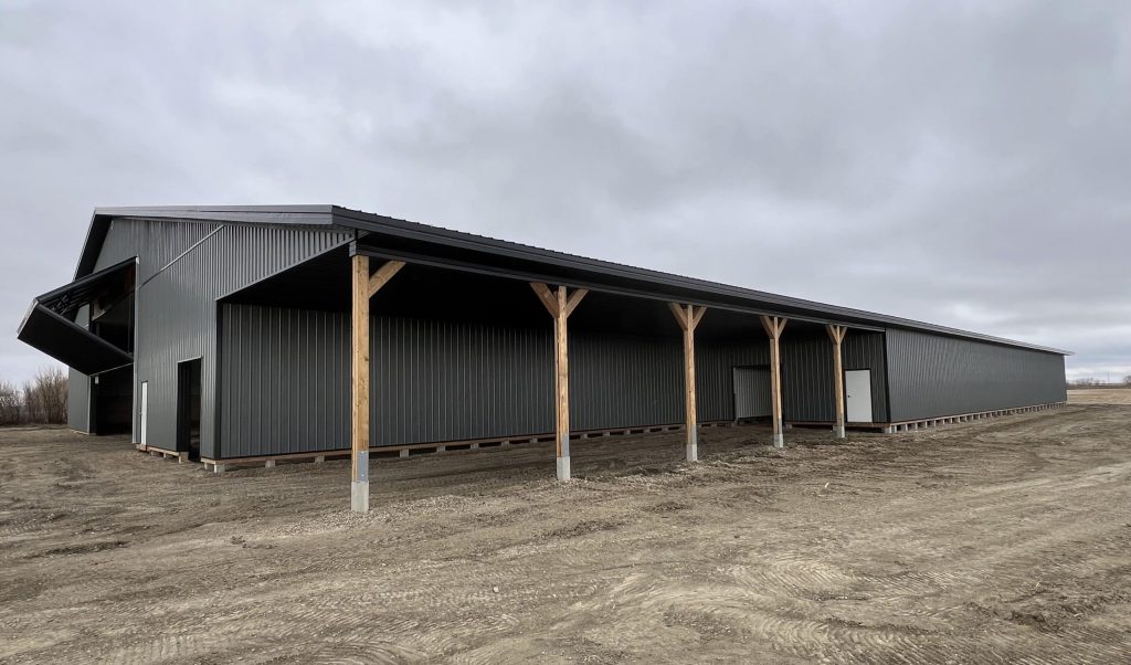 A gunmetal post-frame agricultural storage building with open and closed lean-tos, overhead and bi-fold doors