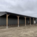 A gunmetal post-frame agricultural storage building with open and closed lean-tos, overhead and bi-fold doors